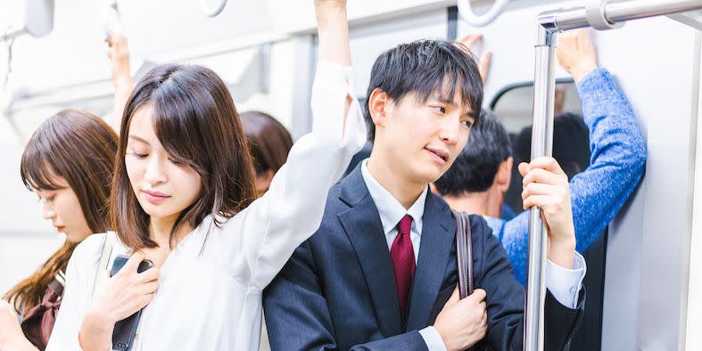 a woman on the subway in japan looking down at her phone while a man stands very closely to her