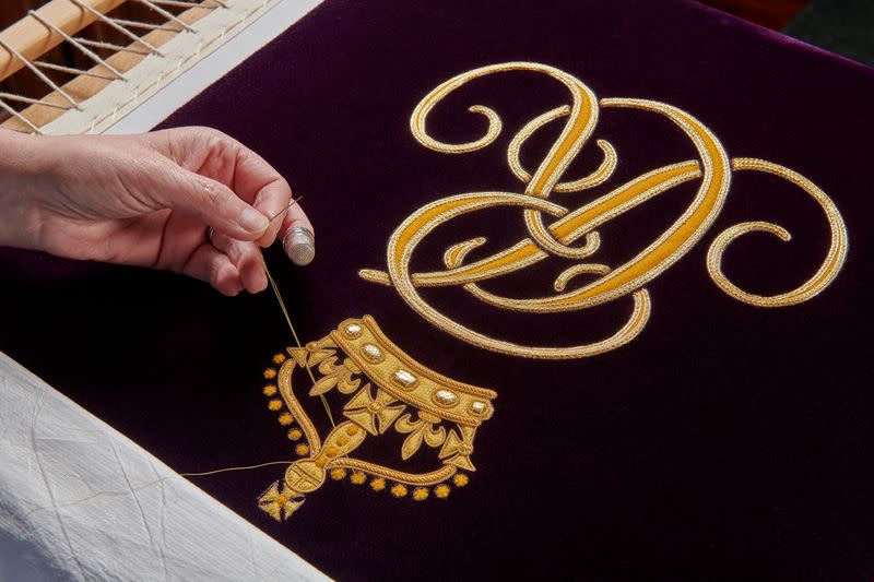 A member of the Royal School of Needlework hand embroiders the Queen Consort's cypher onto her Robe of Estate