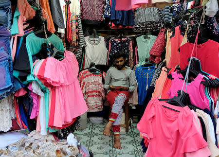 A vendor selling clothes looks at his mobile phone as he waits for customers at a market in Mumbai, India, August 30, 2016. REUTERS/Danish Siddiqui