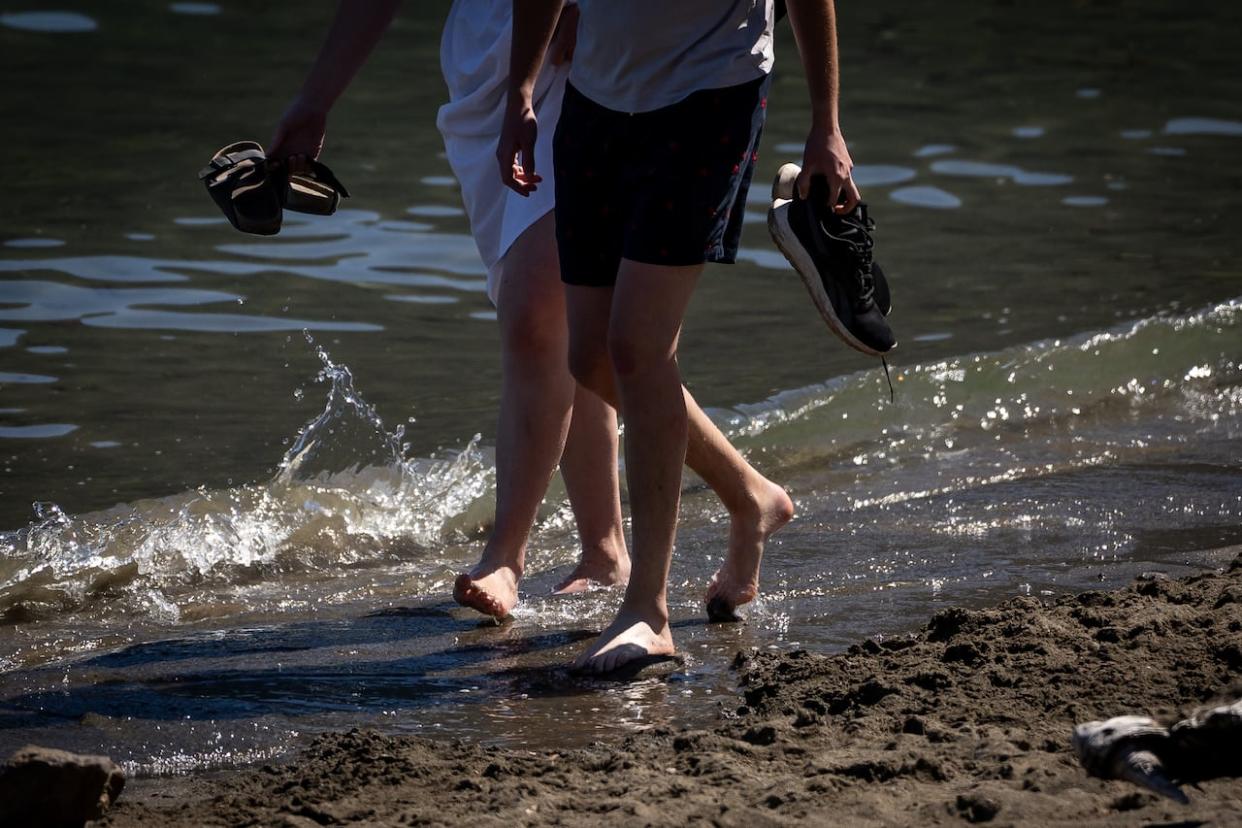 People walk along the beach at Harrison Hot Springs, B.C., on July 5. Heat warnings have been lifted across the South Coast, Lower Mainland and Vancouver Island but remain in place for the southern Interior. (Ethan Cairns/CBC - image credit)