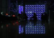 Pedestrians walk past an electronic board showing various stock prices, which are reflected in a polished stone surface, outside a brokerage in Tokyo January 24, 2014. REUTERS/Yuya Shino
