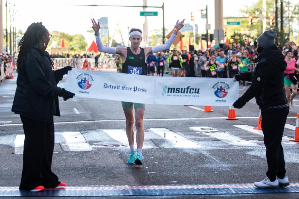 Marathon male winner Mitch Klingler of Jackson crosses the finish line banner held by Free Press Nicole Avery Nichols and MSUFCU president and CEP April Clobes during the 46th?Annual Detroit Free Press Marathon presented by MSU Federal Credit Union?in Detroit on Sunday, Oct. 15, 2023.