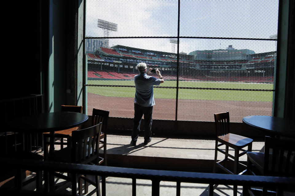 In this June 25, 2020, photo, a reporter photographs the view of the baseball field at Fenway Park from the Bleacher Bar in Boston. Tucked under the center field seats at Fenway Park, down some stairs from Lansdowne Street in an area previously used as the visiting team’s batting cage, is a sports bar that is preparing to reopen from the coronavirus shutdown. If Major League Baseball’s plans remain on schedule, it may be one of the few places fans will be able to watch a game in person this season. (AP Photo/Elise Amendola)