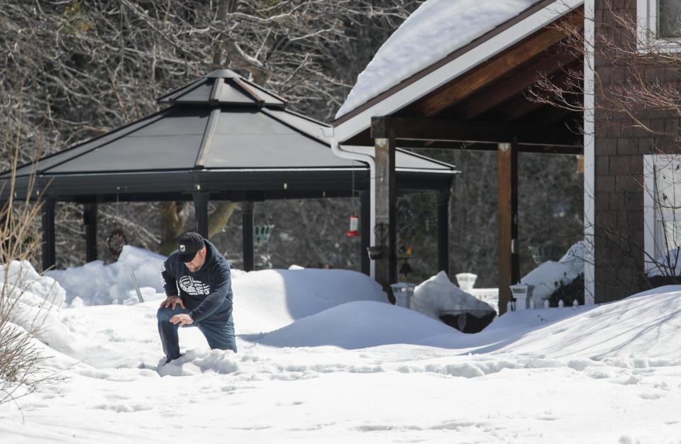 A man kneels in deep snow.