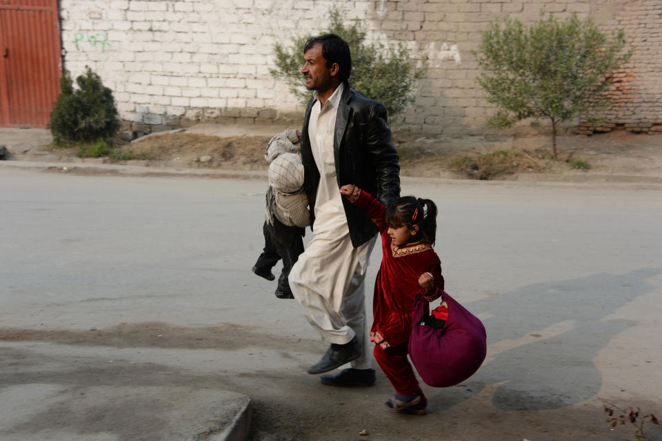 <p>An Afghan man runs with two children near an office of the British charity Save the Children during an ongoing attack in Jalalabad on Jan. 24, 2018. (Photo: Noorullah Shirzada/AFP/Getty Images) </p>