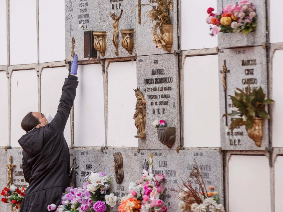 A woman wearing a face mask and gloves touches a niche during the burial of a man who died of the new coronavirus: AFP via Getty Images