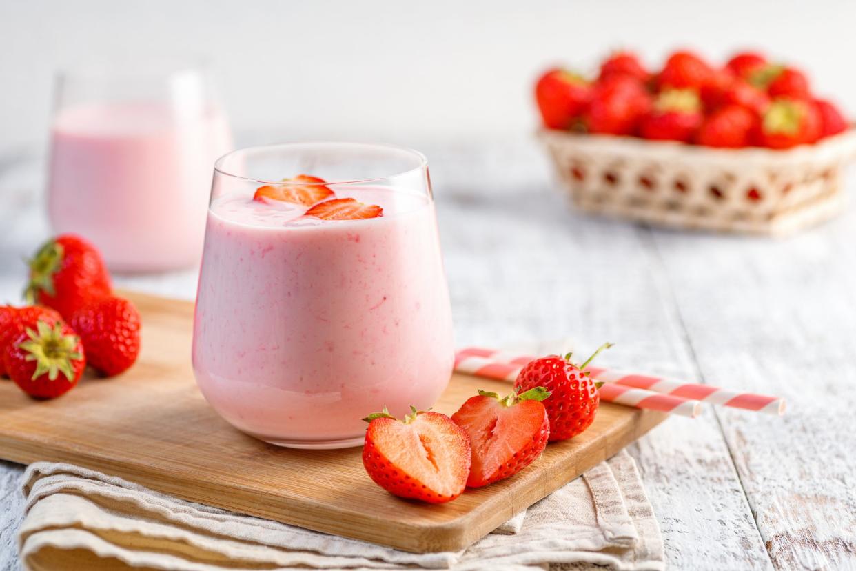 Glass with strawberry smoothie or milkshake on wooden table. Summer drink.