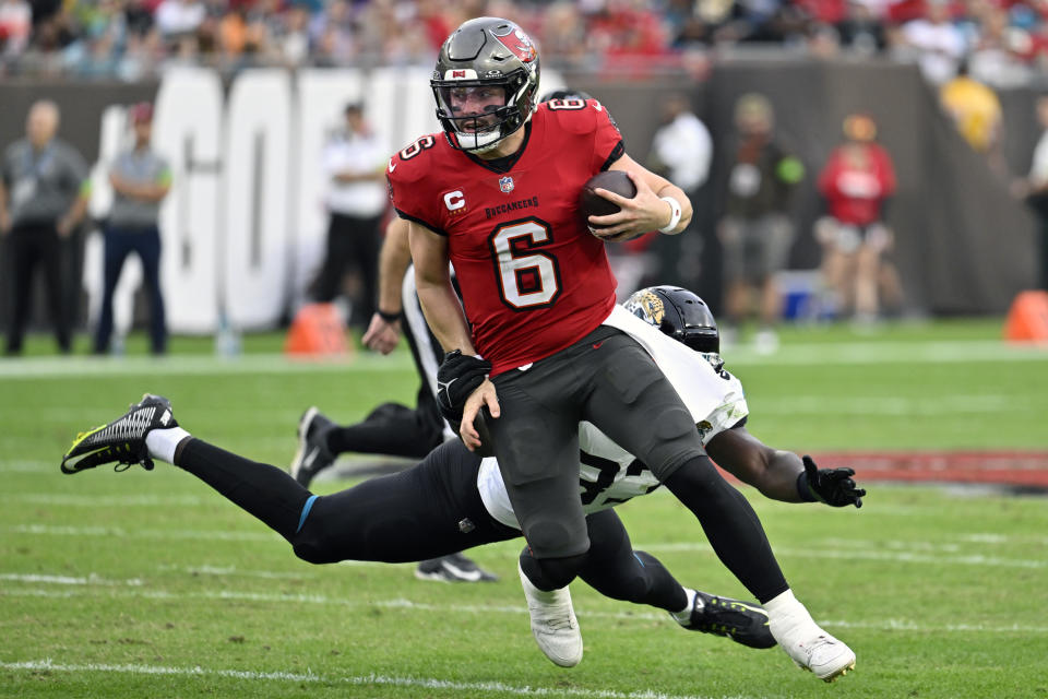 Tampa Bay Buccaneers quarterback Baker Mayfield (6) scrambles past Jacksonville Jaguars linebacker Devin Lloyd during the first half of an NFL football game Sunday, Dec. 24, 2023, in Tampa, Fla. (AP Photo/Jason Behnken)