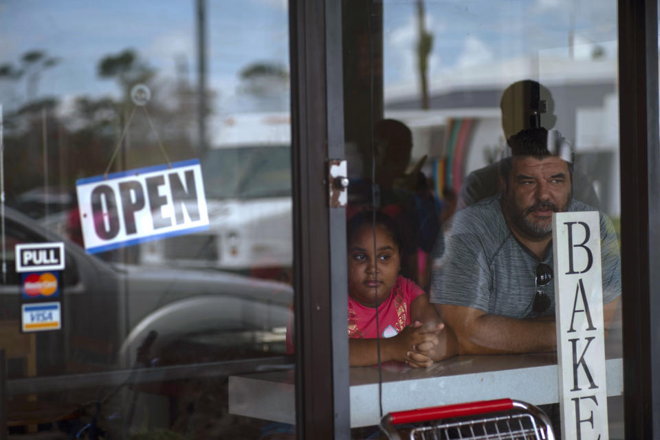 A man and girl peer out from a bakery and cafeteria in Freeport, Bahamas, Wednesday, Sept. 11, 2019. Those who survived Hurricane Dorian are facing the prospect of starting their lives over but with little idea of how or where to even begin. (AP Photo/Ramon Espinosa)