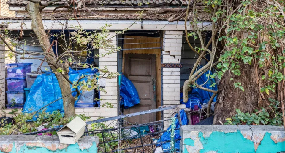 The front gate and front door are broken, and there are boxes of clothes near the entry.