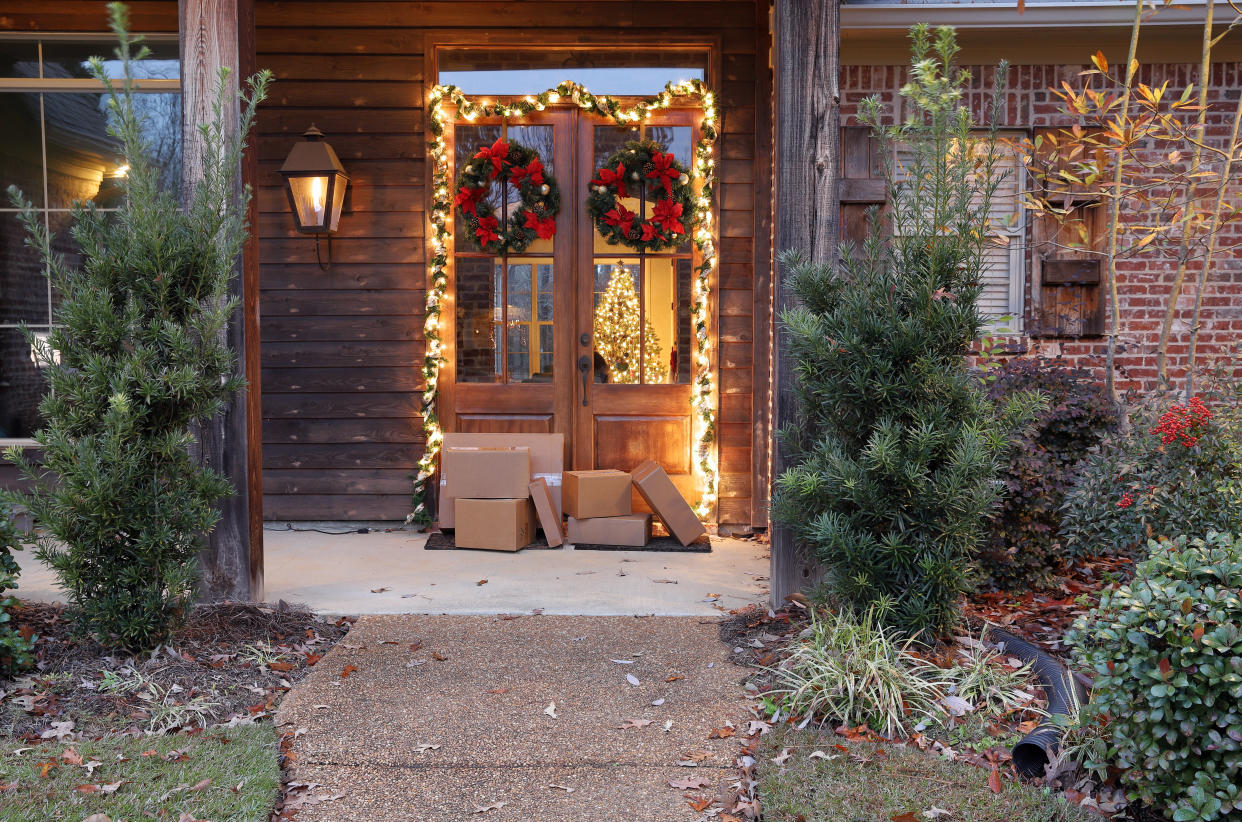 Boxes and packages next to front door during holiday christmas season, with Christmas lights and wreaths