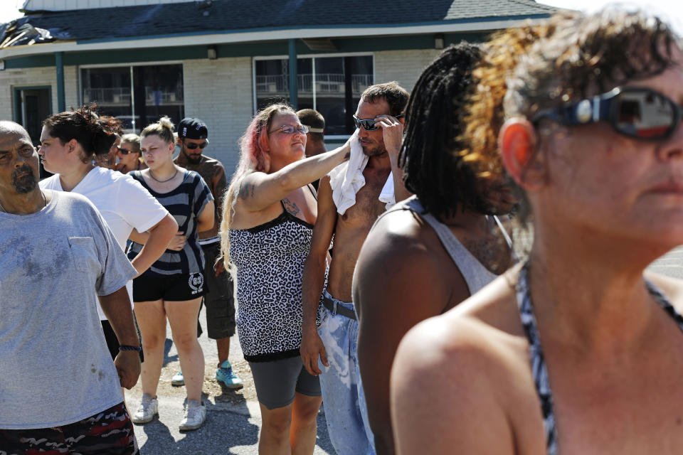 Jeannie, center left, and husband Jason Holcombe wait in the hot sun for food being distributed outside the damaged American Quality Lodge where they continue to live in the aftermath of Hurricane Michael, in Panama City, Fla., Tuesday, Oct. 16, 2018. "Basically, if you were living here before the storm you were homeless. This was our last resort," said Jeannie Holcombe, who has been at the motel a few months with her husband. "It's worse now." (AP Photo/David Goldman)