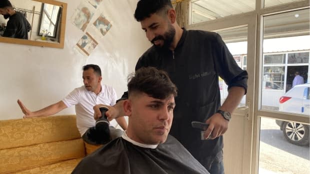 Ibrahim Khalil sits in Sabah Sahdun’s barber chair in the Esyan camp in northern Iraq. Khalil says he no longer feels safe in Iraq so he met with a smuggler who said he could get into the European Union through Belarus.   (Rebecca Collard/CBC - image credit)