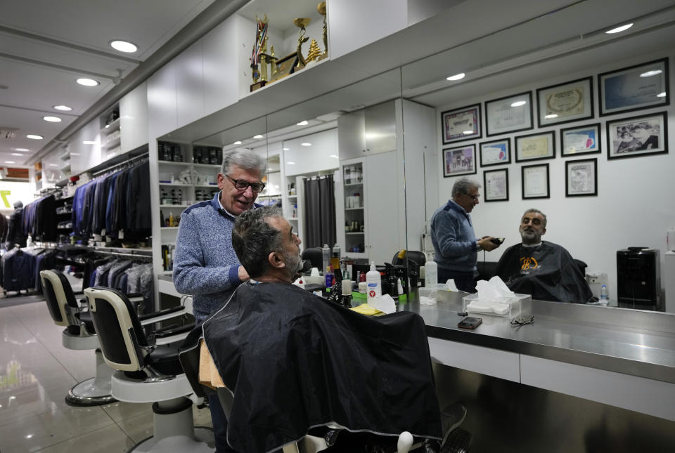 Elie Rbeiz, 70, a hair dresser speaks with a costumer as he shaves for him, at his shop in Hmara street, in Beirut, Lebanon, Friday, Jan. 14, 2022. Rbeiz, who among his clients was late Saudi businessman Adnan Khashoggi, expanded his business 20 years ago to include men clothes. "Hamra is not the Hamra of the past," says the man whose work dropped 60% over the past two years, but still he refuses to leave the country saying this will be equal to suicide for him. (AP Photo/Hussein Malla)