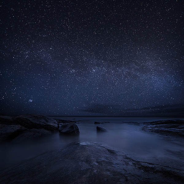 A big, starry sky looms above a rocky coastline. Distant stars illuminate and reflect off a shimmering coastal landscape. <br> <br> <a href="http://www.mikkolagerstedt.com/" rel="nofollow noopener" target="_blank" data-ylk="slk:(Photo by Mikko Lagerstedt);elm:context_link;itc:0;sec:content-canvas" class="link ">(Photo by Mikko Lagerstedt)</a>