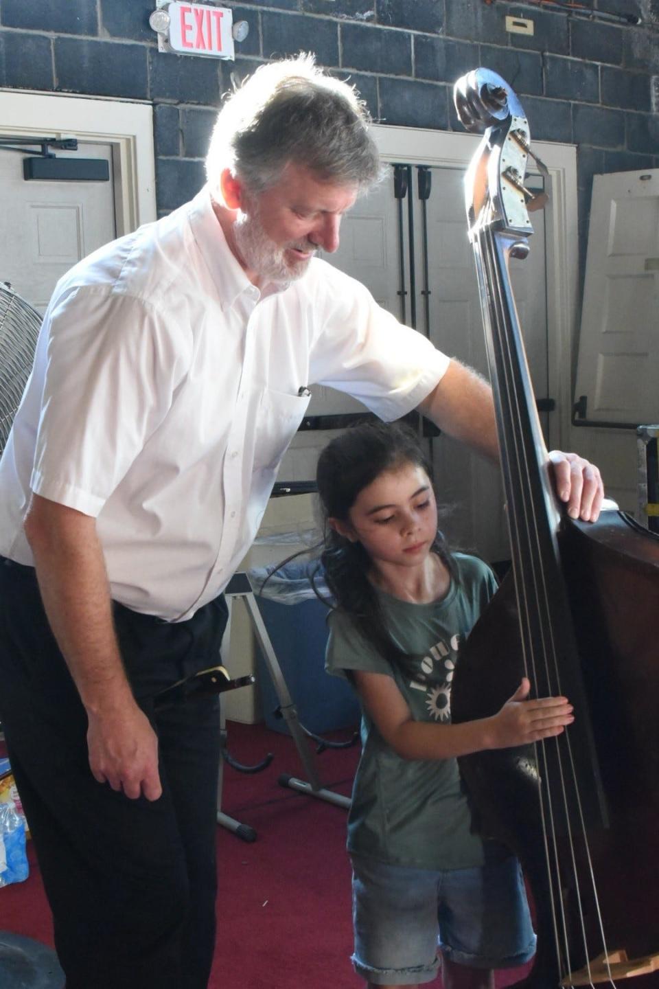 Lakeside Symphony Orchestra member Aaron Keaster, of Perrysburg, watches over Sofia Beverly, age 7, of Port Clinton, as she tries out the double bass at Hoover Auditorium in Lakeside.