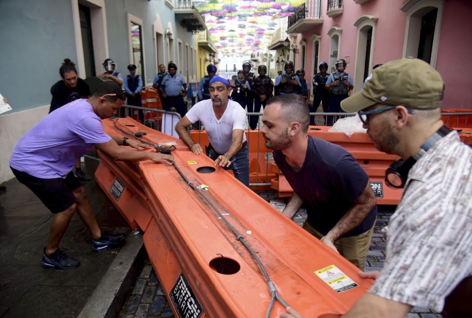 Protesters remove street barricades that are filled with water as police block them from reaching La Fortaleza governor's residence in San Juan, Puerto Rico, Sunday, July 14, 2019. Protesters are demanding Gov. Ricardo Rosselló step down for his involvement in a private chat in which he used profanities to describe an ex-New York City councilwoman and a federal control board overseeing the island's finance. (AP Photo/Carlos Giusti)