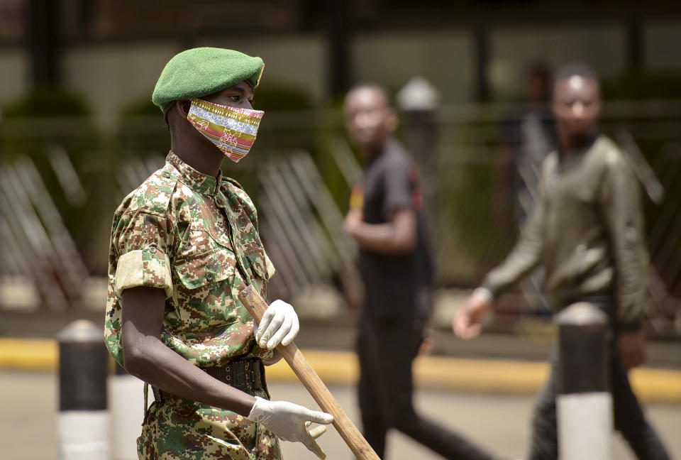 A member of the Kenya Youth Service wears a cloth face mask as he keeps members of the public at a distance as volunteers disinfect a road in an attempt to curb the spread of the new coronavirus, in downtown Nairobi, Kenya Friday, April 3, 2020. The new coronavirus causes mild or moderate symptoms for most people, but for some, especially older adults and people with existing health problems, it can cause more severe illness or death. (AP Photo/John Muchucha)