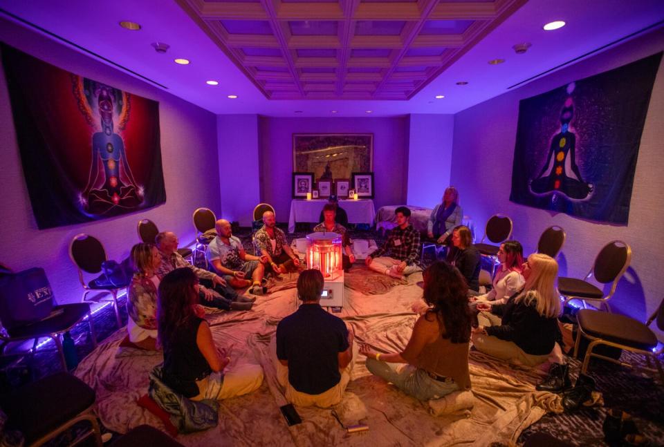 A circle of people sitting cross-legged on the floor in a room with glowing purple light