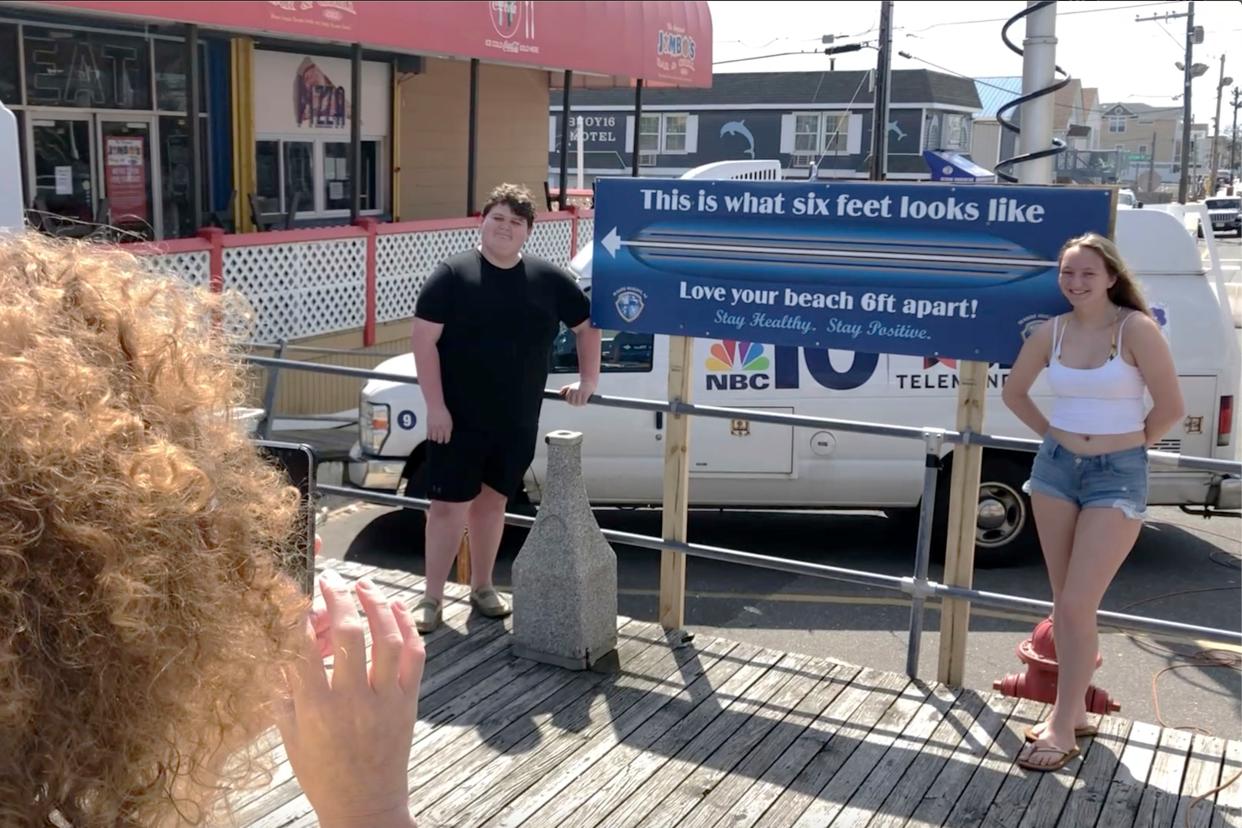 Two people pose for a picture with a social distancing sign on the boardwalk at Seaside Heights, N.J. on Friday, May 15, 2020, the first day the beach and boardwalk were during the coronavirus outbreak.