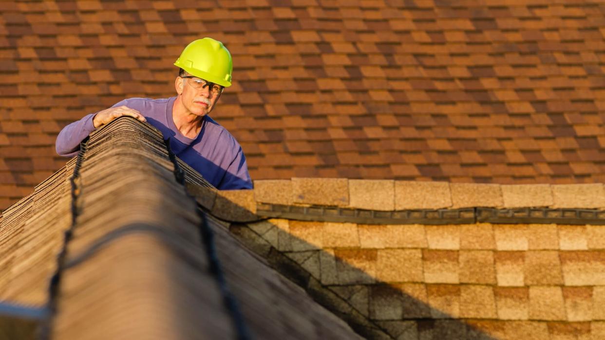 An inspector looks over a residential roof at the peak.