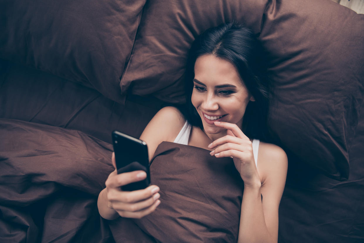 Woman lying in bed looking at dating app on mobile phone 