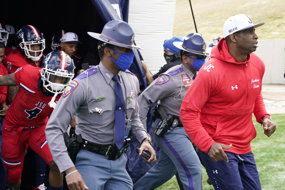 Jackson State football coach Deion Sanders, right, leads an accompanying security detail and his team onto the field prior to the first half of an NCAA college football game against Edward Waters in Jackson, Miss., Sunday, Feb. 21, 2021. The game marks Sanders's collegiate head coaching debut. (AP Photo/Rogelio V. Solis)