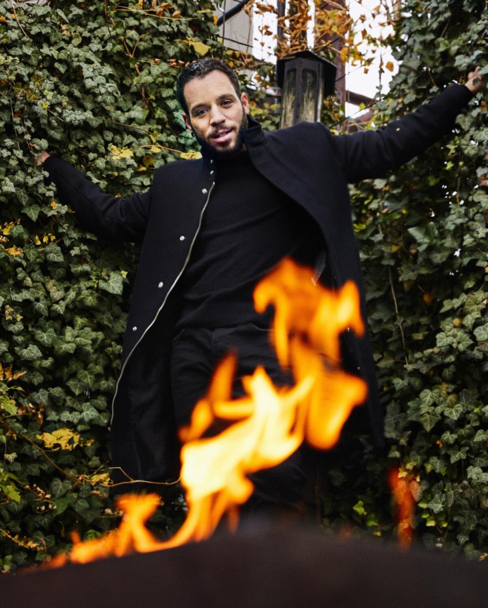 Actor Robin de Jesus jumps near an outdoor fire pit.