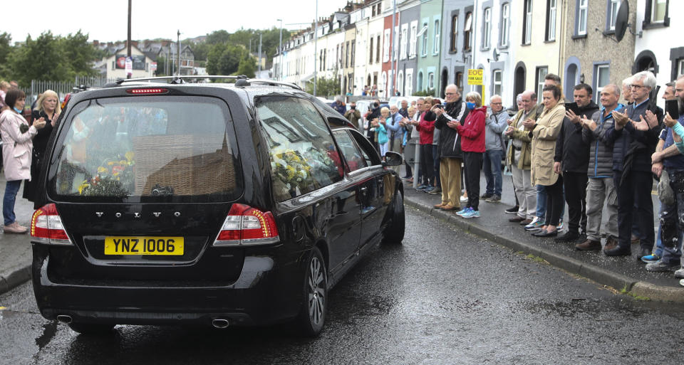 The funeral cortege of the former Northern Ireland lawmaker and Nobel Peace Prize winner John Hume passes through the streets as people bow their heads following the funeral Mass at St Eugene's Cathedral in Londonderry, Northern Ireland, Wednesday, Aug. 5, 2020. Hume was co-recipient of the 1998 Nobel Peace Prize with fellow Northern Ireland lawmaker David Trimble, for his work in the Peace Process in Northern Ireland. Masks are worn due to the ongoing Coronavirus outbreak . (AP Photo/Peter Morrison)