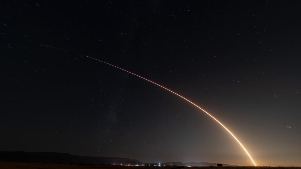  A rocket launch carves an orange arc into a dark night sky in this long-exposure photo. 