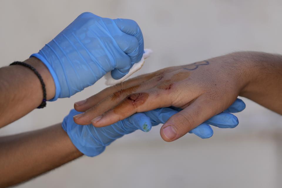 A volunteer gives the first aid to an injured Afghan migrant at an old school used as a temporary shelter on the island of Kythira, southern Greece, Thursday, Oct. 6, 2022. Bodies floated amid splintered wreckage in the wind-tossed waters off a Greek island Thursday as the death toll from the separate sinkings of two migrant boats rose to 22, with many still missing. (AP Photo/Thanassis Stavrakis)