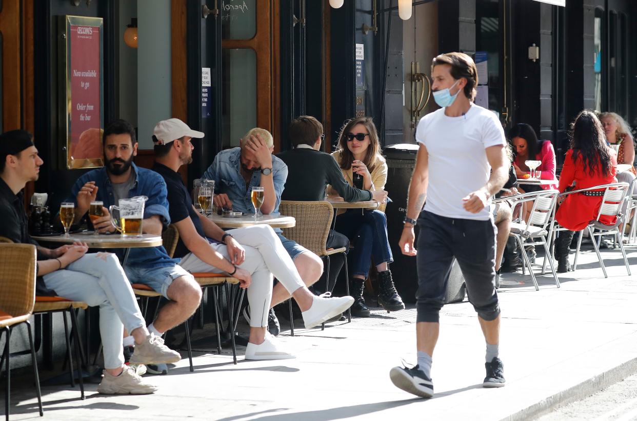 A man wearing a face mask or covering due to the COVID-19 pandemic, walks past consumers sat outside a restaurant in London on August 3, 2020, as the Government's "Eat out to Help out" coronavirus scheme to get consumers spending again gets underway. - Britain's "Eat out to Help out" scheme began Monday, introduced last month by Chancellor Rishi Sunak to help boost the economy claw its way from a historic decline sparked by the coronavirus crisis. (Photo by Tolga AKMEN / AFP) (Photo by TOLGA AKMEN/AFP via Getty Images)