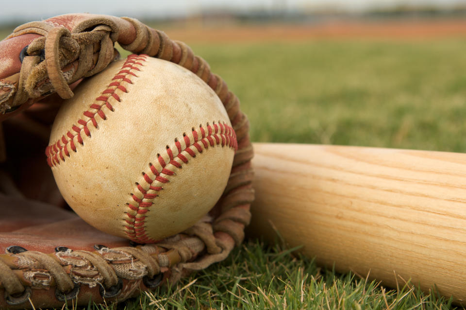 A baseball in a glove and baseball bat laying in grass.