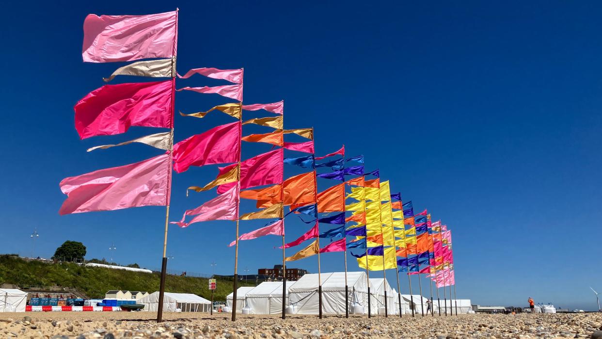 Multi-coloured flags ripple in the breeze in front of white marquees at Lowestoft beach