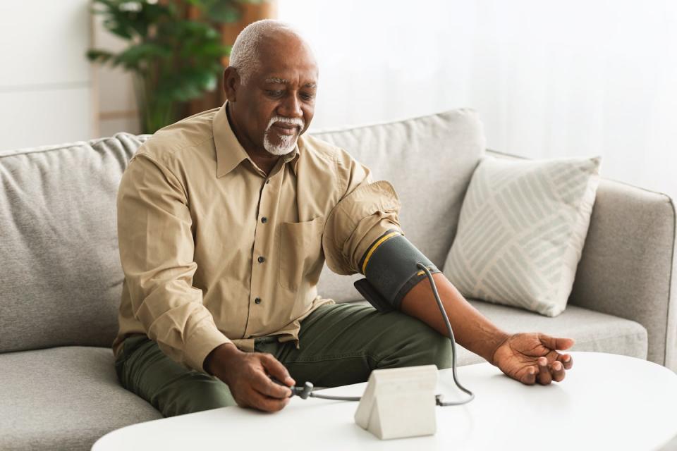 A man with gray hair using a blood pressure monitor at home.