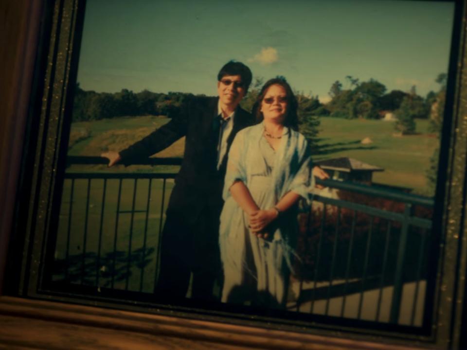 hann pan and bich pan seen in a photo, displayed in a frame on a table. the two are standing in front of a green field, leaning against a railing, and smiling.