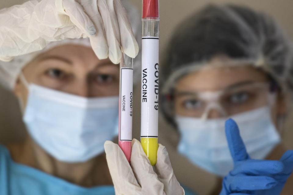 People in protective suits and face masks look at test tubes with samples of the vaccine against the coronavirus. (Photo illustration by Maxym Marusenko/NurPhoto via Getty Images)