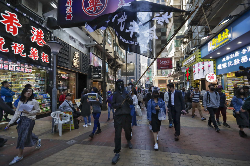 A pro-democracy protester waves a flag as protesters and office workers march past business shop lots during a protests at Causeway Bay in Hong Kong, Wednesday, Dec. 11, 2019. Hong Kong Chief Executive Carrie Lam on Tuesday again ruled out further concessions to protesters who marched peacefully in their hundreds of thousands this past weekend, days before she is to travel to Beijing for regularly scheduled meetings with Communist Party leaders. (AP Photo/Mark Schiefelbein)