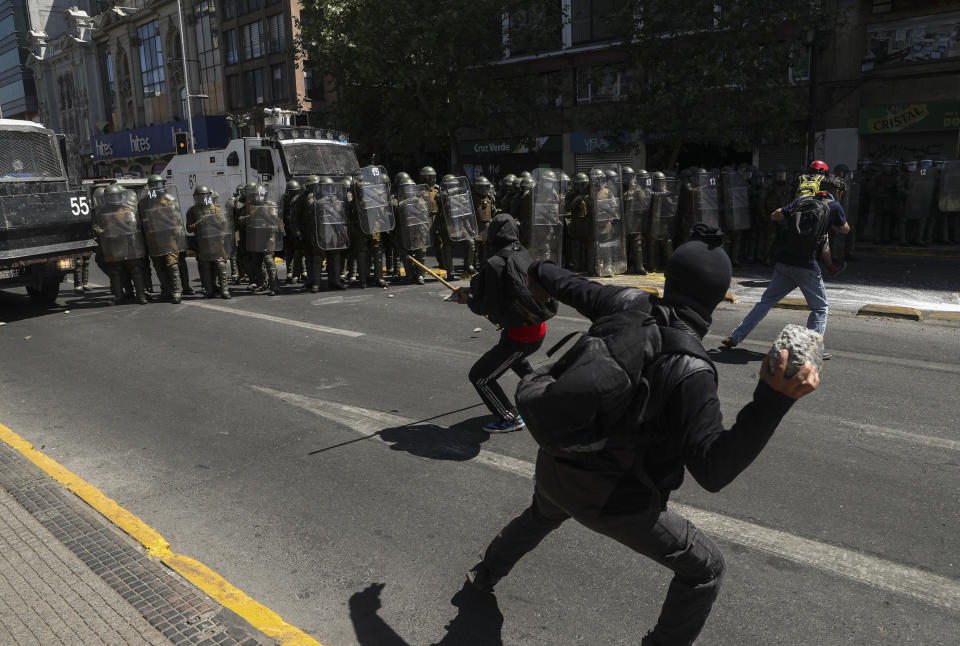 A protester aims a rock at police trying to disperse a march against the commemoration of the discovery of the Americas, organized by indigenous groups demanding autonomy and the recovery of ancestral land in Santiago, Chile, Monday, Oct. 12, 2020. (AP Photo/Esteban Felix)