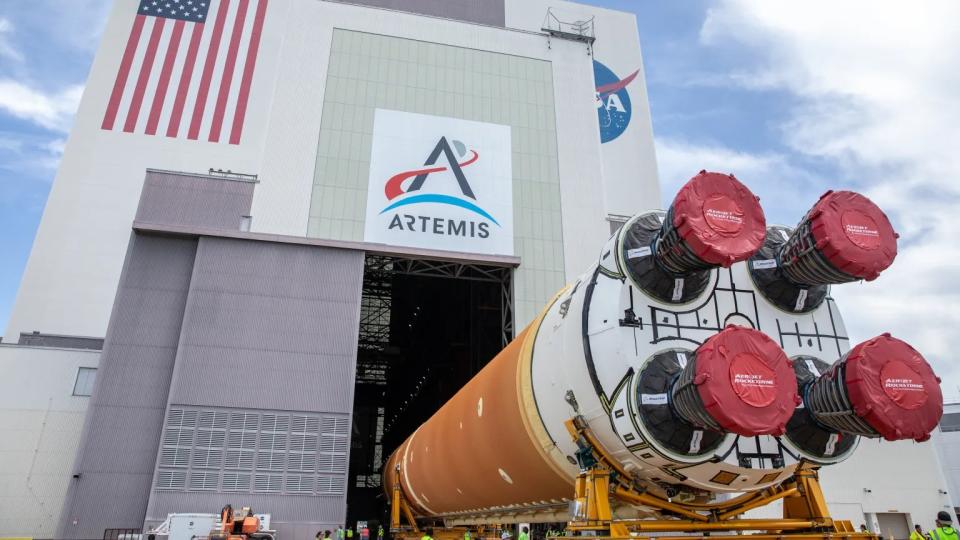  A rocket on its side going into a large building that has banners for the artemis program, the u.s. flag and nasa at the top. 