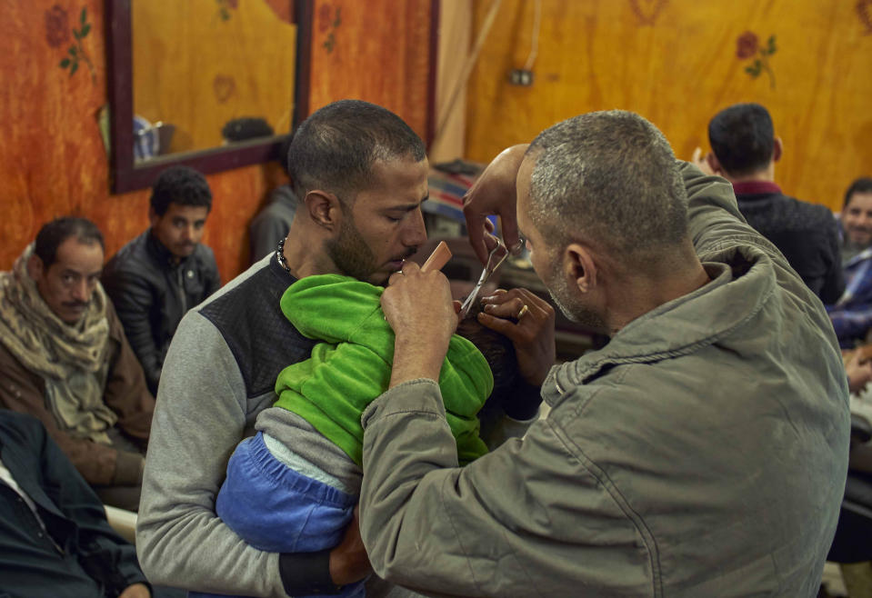 Romany, a Coptic man, left, holds his four-year-old son, for Eissa the barber to cut his hair, in preparation for the Coptic Christmas celebration, at a residential and industrial area of eastern Cairo, Egypt, Monday, Jan. 6, 2020. (AP Photo/Hamada Elrasam)