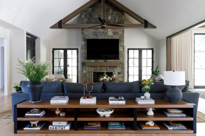 This farmhouse-style living room by Becky Shea incorporates large, comfy furniture, exposed beams, and a stone fireplace.