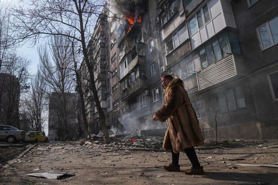 FILE: A woman walks past a burning apartment building after shelling in Mariupol, Ukraine (AP)