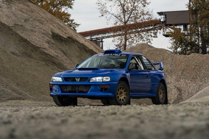 front three-quarter view of a blue Subaru 2.5RS coupe parked among piles of gravel in an industrial setting.