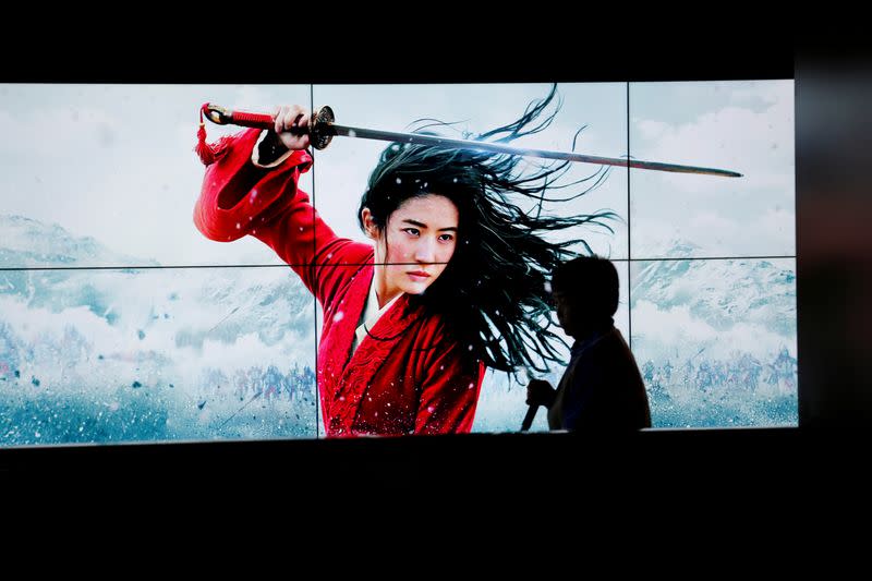 FILE PHOTO: Cleaner walks past screens promoting Disney's movie "Mulan" as the film opens in China, at a cinema in Beijing