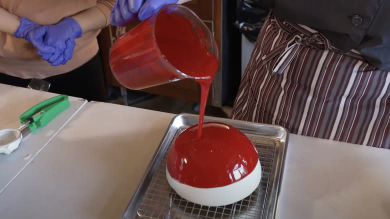 pouring red glaze on dome cake