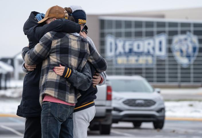 (Left to right) Alexis Lewis of Oxford, Matt McMahon of Hadley, Garrett Latta of Oxford and Mama Ross of Oxford hug while visiting a memorial being built at an entrance to Oxford High School on December 1, 2021, following an active shooter situation at Oxford High School that left four students dead and multiple others with injuries.