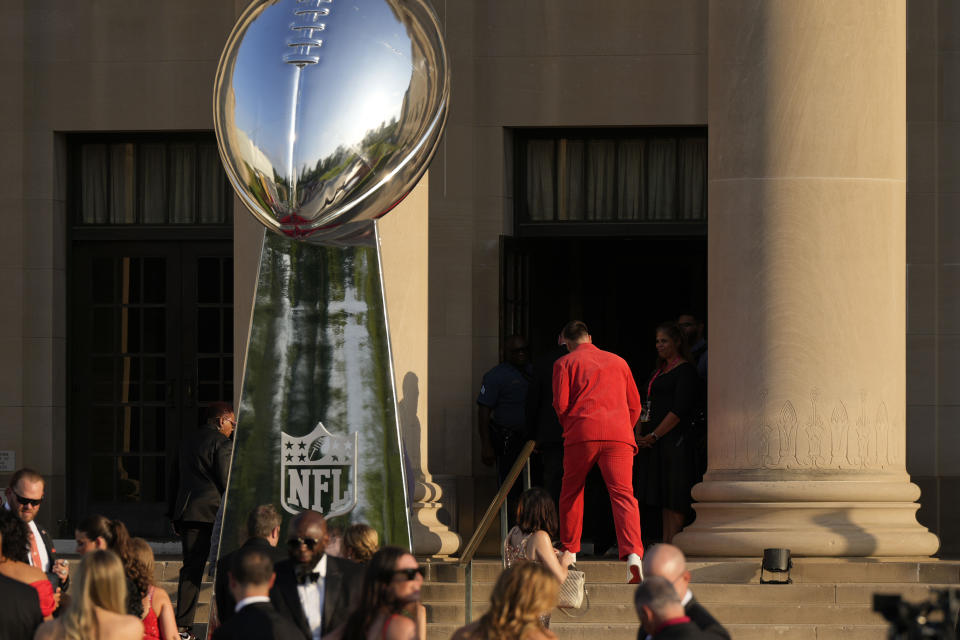 Wearing a bright red suit, Kansas City Chiefs tight end Travis Kelce enters the The Nelson-Atkins Museum of Art for a ceremony for team members to receive their championship rings for winning NFL's Super Bowl 58 football game Thursday, June 13, 2024, in Kansas City, Mo. (AP Photo/Charlie Riedel)