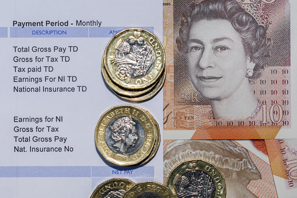 London, UK: July 25, 2018: Pay Slip with British one pound coins with a ten pound note background indicating a monthly payment in a horizontal format.