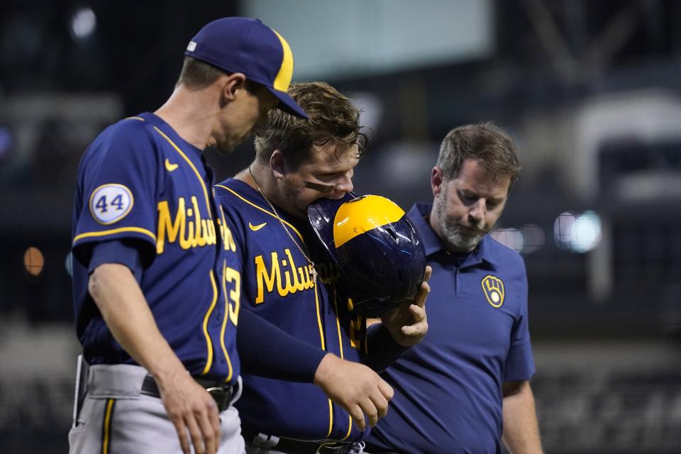 After scoring a run, Milwaukee Brewers' Daniel Vogelbach, middle, bites his helmet due to the pain of an injured leg as he is helped off the field by Brewers manager Craig Counsell, left, and Brewers assistant athletic trainer Dave Yeager, right, during the sixth inning of a baseball game against the Arizona Diamondbacks Tuesday, June 22, 2021, in Phoenix. (AP Photo/Ross D. Franklin)